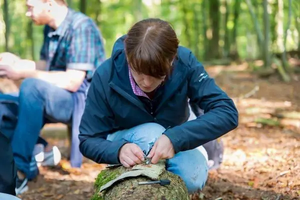 Frau bearbeitet Rinde mit einem Messer auf einem Baumstamm im Wald
