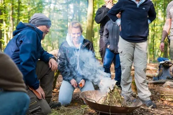 Frau entzündet Zunder in einer Feuerstelle, Rauch steigt auf