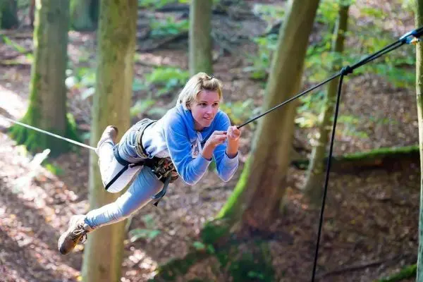 Frau schwingt an einer Seilbrücke zwischen Bäumen im Wald