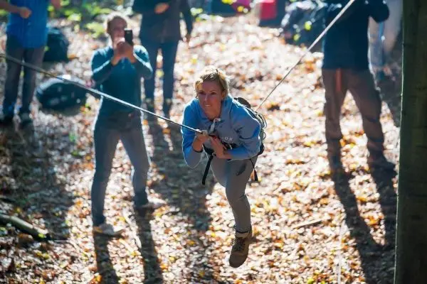 Frau schwingt an Seilbrücke durch den Wald, Zuschauer beobachten