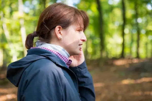 Frau telefoniert im Wald, umgeben von Bäumen und herbstlichem Laub