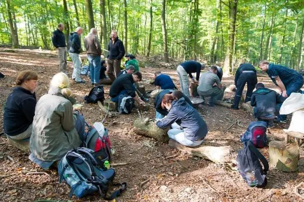 Gruppe arbeitet am Boden im Wald mit Rucksäcken beim Überlebenstraining