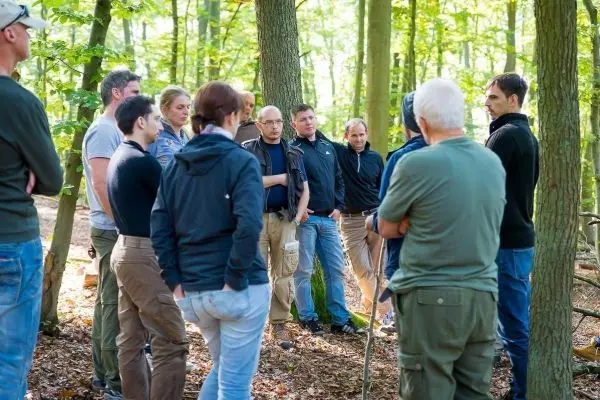 Gruppe diskutiert im Wald, einige halten Stöcke in der Hand