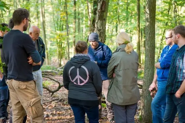 Gruppe hört einem Trainer im Wald aufmerksam zu beim Überlebenstraining