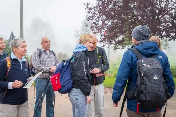 Gruppe mit Rucksäcken und Karten bespricht Wanderroute in nebliger Umgebung