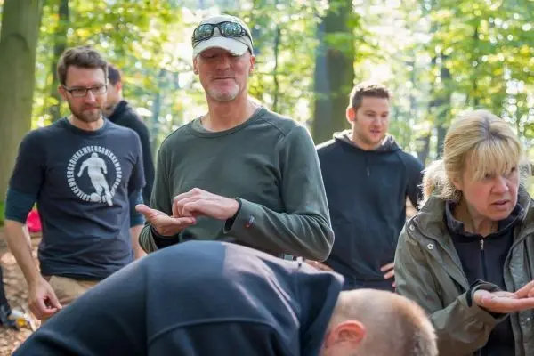 Gruppe übt praktische Fähigkeiten im Wald, einige Personen schauen auf ihre Hände