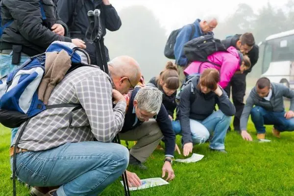 Gruppe von Personen betrachtet Karten auf dem Gras beim Outdoortraining