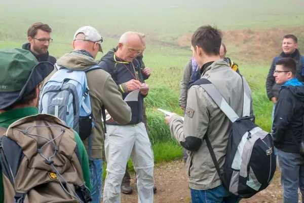 Gruppe von Personen diskutiert auf einem Weg, einige halten Karten oder Notizen
