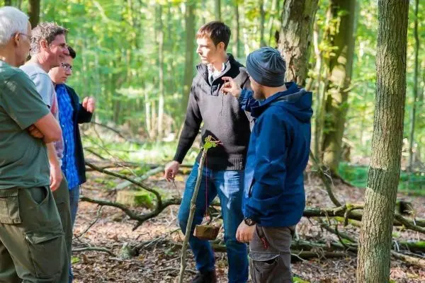 Gruppe von Personen diskutiert im Wald über eine selbstgebaute Vorrichtung