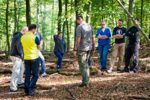 Gruppe von Personen hört einem Trainer im Wald zu