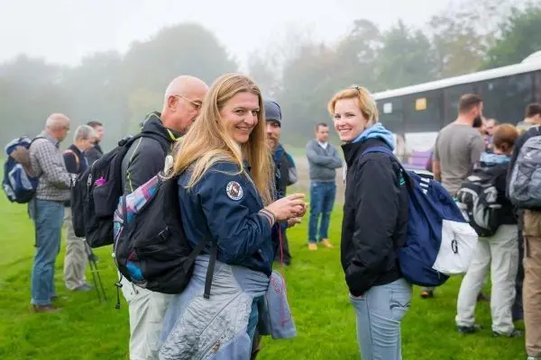 Gruppe von Personen mit Rucksäcken steht auf einer Wiese in nebliger Umgebung