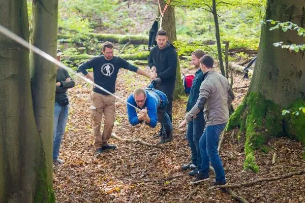 Gruppe von Personen sichert einen Mann an einer Seilbrücke im Wald