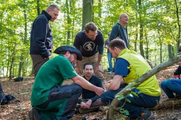 Gruppe von Personen sitzt im Wald und diskutiert über eine Holzarbeit