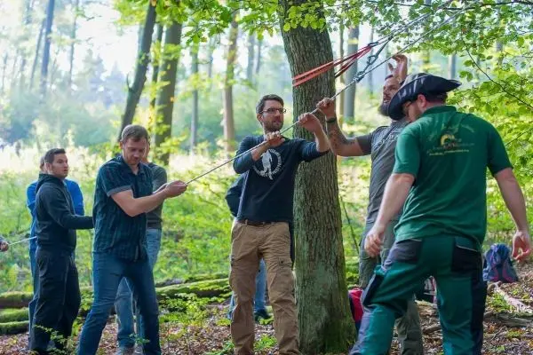Gruppe von Personen spannt Seil um Baum im Wald
