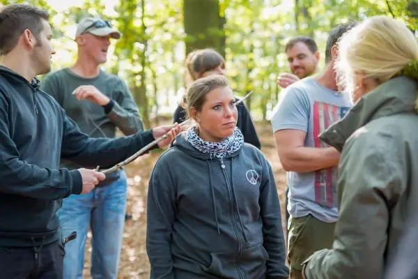 Gruppe von Personen steht im Wald und diskutiert miteinander beim Survival Training
