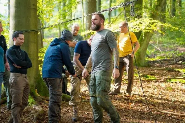 Gruppe von Personen übt an einer selbstgebauten Seilbrücke im Wald