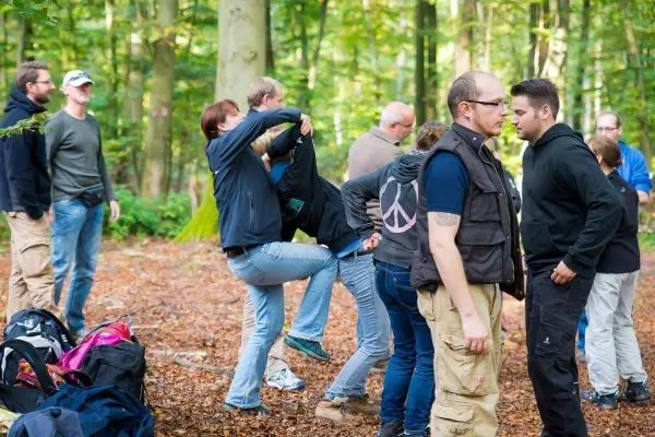 Gruppenteilnehmer üben eine Technik in einem Waldgebiet mit Rucksäcken im Hintergrund