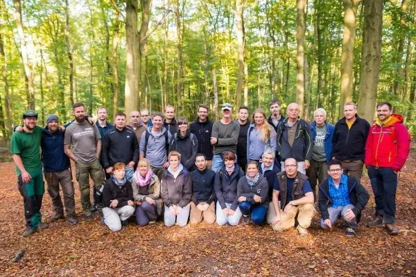 Gruppierung von Personen im Wald auf Laubboden, umgeben von Bäumen