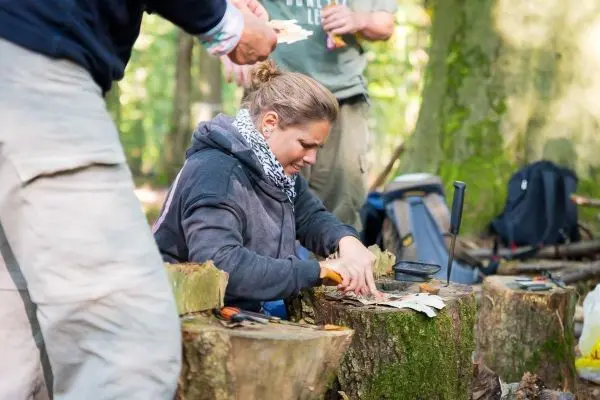 Holz wird mit einem Messer bearbeitet, während eine Person Unterstützung bietet