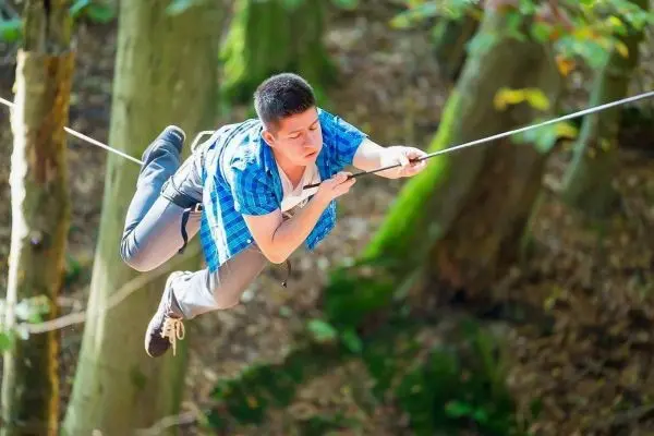 Junge schwingt an einer Seilbrücke zwischen Bäumen im Wald