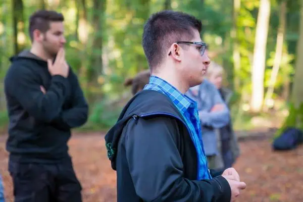 Junger Mann mit Brille steht im Wald und hört aufmerksam zu