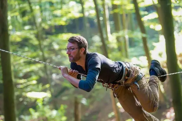 Kletterer schwingt an einer Seilbrücke zwischen Bäumen im Wald