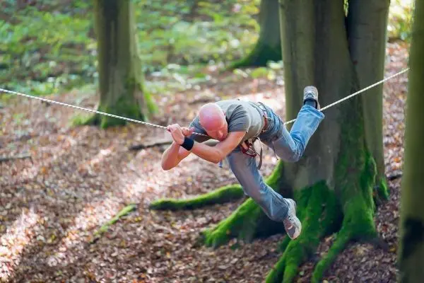 Kletterer schwingt an einer Seilbrücke zwischen zwei Bäumen