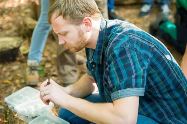 Mann bearbeitet mit einem Messer Materialien aus einer Kunststoffbox im Wald