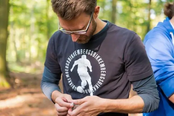Mann befestigt Ausrüstung an seinem T-Shirt im Wald