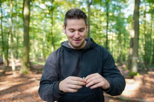 Mann hält einen kleinen Gegenstand zwischen den Fingern im Wald