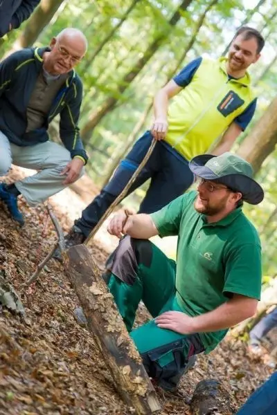 Mann kniet neben einem Holzstück und bearbeitet es mit einem Messer