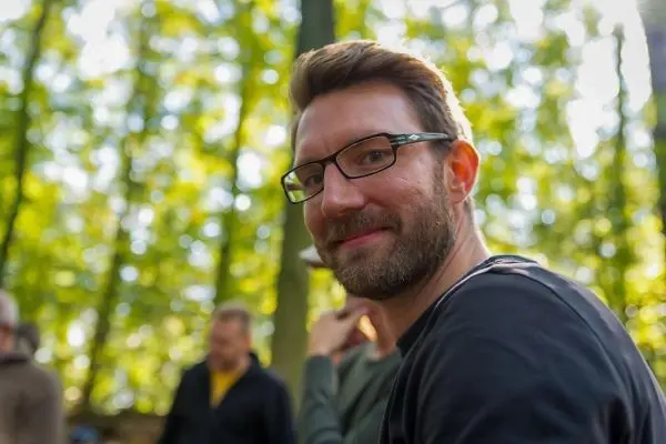 Mann mit Brille sitzt im Wald und lächelt in die Kamera