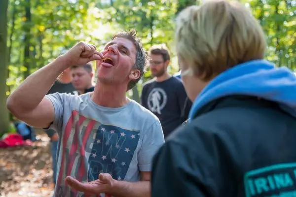 Mann probiert essbare Pflanze im Wald, während andere Teilnehmer zuschauen