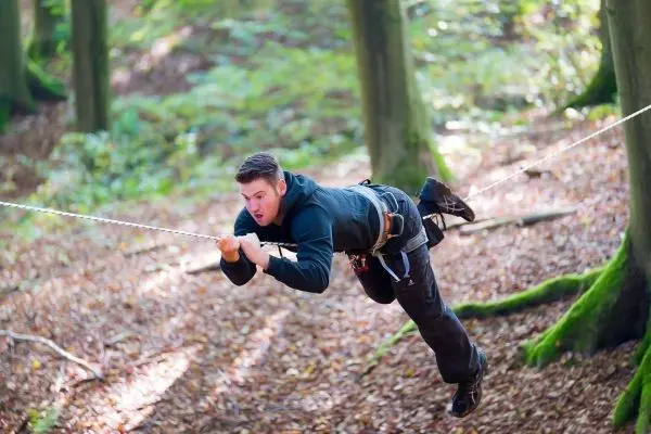 Mann schwingt an einem Seil zwischen Bäumen im Wald