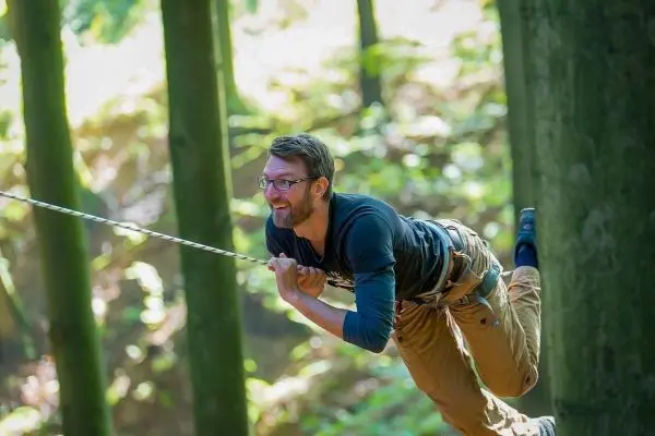Mann schwingt an einer Seilbrücke zwischen Bäumen im Wald