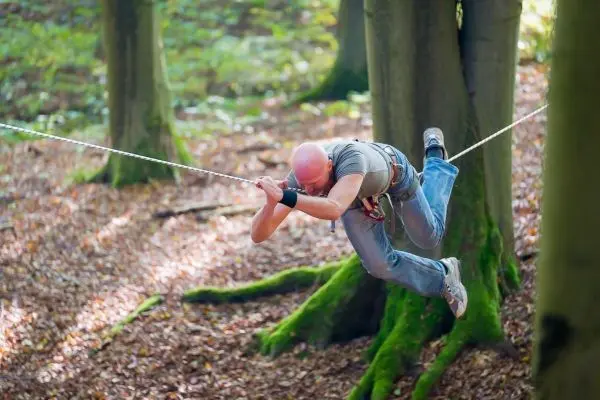 Mann schwingt an einer Seilbrücke zwischen Bäumen im Wald
