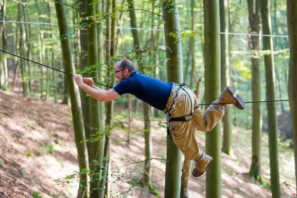 Mann schwingt an einer Seilbrücke zwischen Bäumen im Wald