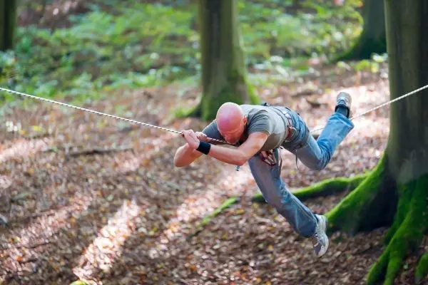 Mann schwingt an einer Seilbrücke zwischen Bäumen im Wald