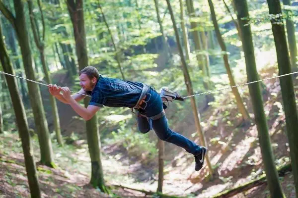 Mann schwingt an einer Seilbrücke zwischen Bäumen im Wald