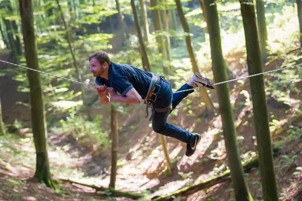 Mann schwingt an einer Seilbrücke zwischen Bäumen im Wald