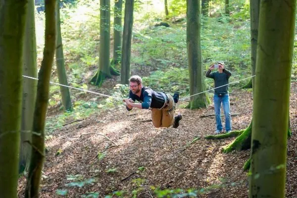 Mann schwingt an einer Seilbrücke zwischen Bäumen im Wald
