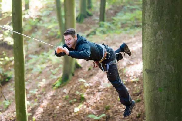 Mann schwingt an einer Seilbrücke zwischen zwei Bäumen