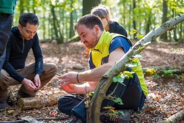 Mann sitzt auf dem Boden und nutzt ein Smartphone, während andere im Hintergrund arbeiten