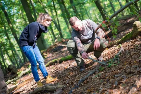 Mann untersucht den Boden im Wald, während Frau aufmerksam zuschaut