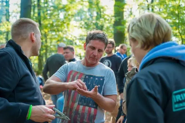 Mann zeigt anderen Teilnehmern eine Technik mit einem Werkzeug im Wald