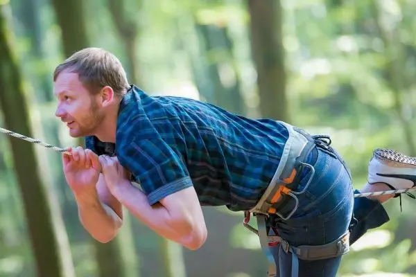 Mann zieht sich an einem Seil in den Wald hoch