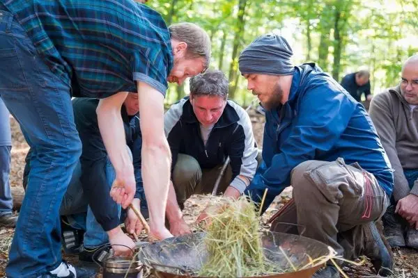 Mehrere Personen bereiten Zunder in einer Feuerstelle im Wald vor