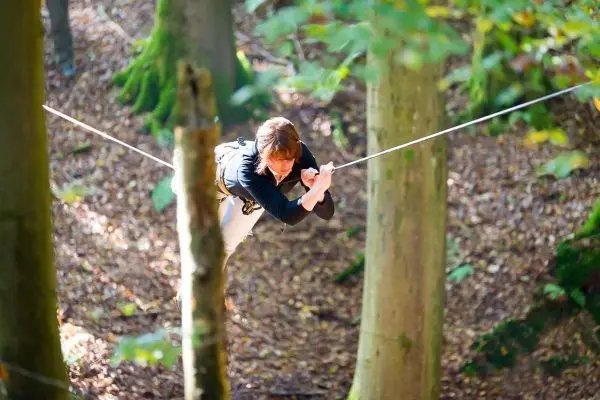 Person balanciert auf einer gespannten Seilbrücke zwischen Bäumen