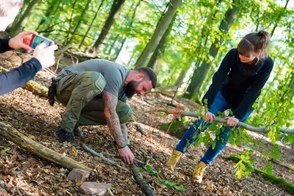 Person bindet Äste zusammen, Person hält einen Stock fest beim Überlebenstraining
