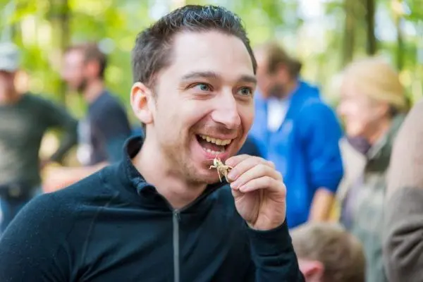 Person hält ein Insekt vor den Mund und lächelt
